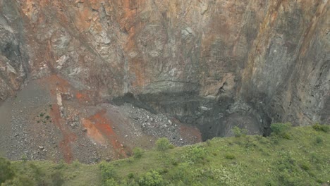 Aerial-tilt-looks-over-rim-into-big-hole-at-Cullinan-Diamond-Mine,-ZA