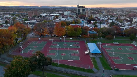 Toma-Aérea-De-Un-Camión-De-Hombres-Jugando-Baloncesto-En-Un-Parque-Urbano-Rodeado-De-Follaje-Colorido-En-Otoño