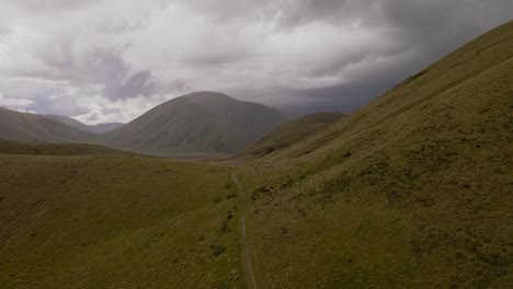 Empty-path-leading-over-a-ridge-line-in-mountainous-wilderness-underneath-dark-and-heavy-storm-clouds