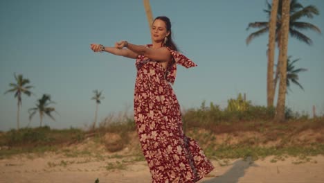 Eine-Attraktive-Kaukasische-Frau,-Die-Sich-Bückt,-Um-Eine-Handvoll-Strandsand-Aufzuheben,-Während-Sie-Den-Sand-Zwischen-Ihren-Fingern-Fallen-Lässt-Und-Den-Morgendlichen-Sonnenaufgang-Und-Die-Freiheit-Genießt,-In-Der-Natur-Zu-Sein