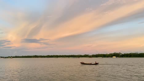 Ein-Fischerboot-überquert-Den-Fluss-Gegen-Die-Bewölkte-Sonnenuntergangskyline