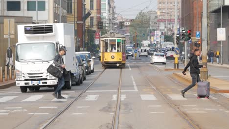 La-Gente-Camina-En-El-Cruce-De-Peatones-Con-Coches-Y-Tranvías-En-El-Fondo,-Centro-De-La-Ciudad-De-Milán