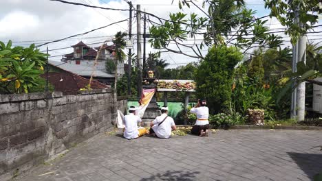 Balinesische-Hindu-Familie-Betet-In-Einem-Straßentempel-In-Gianyar,-Sukawati,-Bali,-Indonesien,-Und-Hebt-Ihre-Hände-Vor-Den-Opfergaben