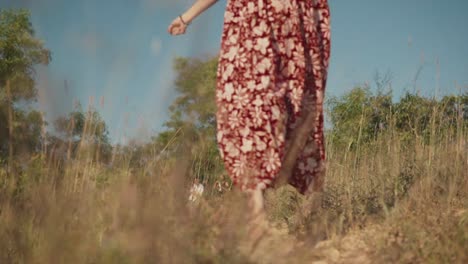 Una-Toma-En-Cámara-Lenta-De-Una-Atractiva-Mujer-Caucásica-Con-Un-Vestido-Floral-Rojo,-Felizmente-Saltando-Y-Corriendo-Por-Un-Camino-Despreocupado-En-Un-Campo-Al-Aire-Libre,-India