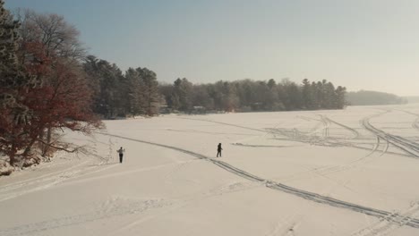 Aerial-of-two-people-cross-country-skiing-on-a-snow-covered-frozen-lake-during-winter