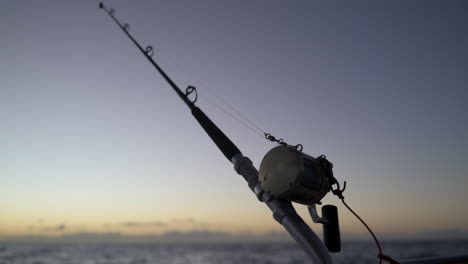 Slow-motion-shot-of-a-fishing-rod-against-a-the-backdrop-of-a-rising-sun-on-the-pacific-ocean