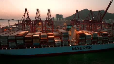 Rote-Portalkräne-Moderner-Frachtterminals,-Die-Kurz-Nach-Sonnenuntergang-In-Hongkong-Ein-Schiff-Der-Maersk-Linie-Entladen