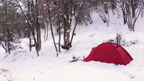 Hombre-Columpiándose-En-Una-Hamaca-Disfrutando-De-La-Nieve-Cerca-De-Su-Tienda-En-El-Campamento-De-Invierno