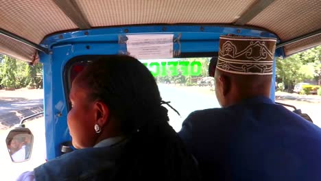 Two-african-people-sitting-in-a-typical-tuk-tuk-in-town-of-Mto-wa-Mbu,-handheld