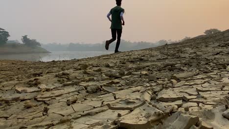 Establisher-shot-of-empty-dry-land-with-man-sprinting-away-from-camera,-misty