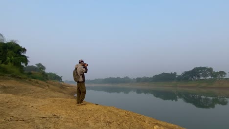 Wide-shot-of-single-male-Photographer-taking-pictures-of-polluted-river,-dolly-zoom-in-shot
