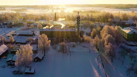 Small-village-on-cold-winter-morning-golden-sunrise-with-smoking-chimneys,-aerial-opening-scene