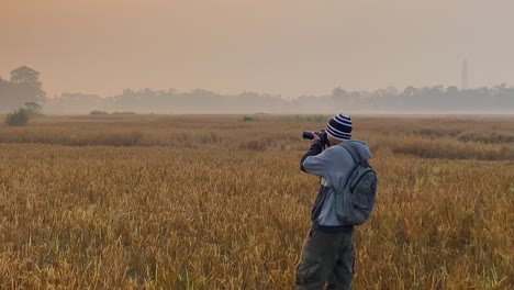 Profile-wide-view-of-photographer-on-field-taking-pictures-of-polluting-industry