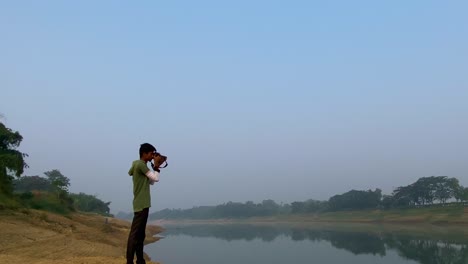Bangladeshi-young-man-taking-picture-of-polluted-river,-misty-morning,-zoom-out