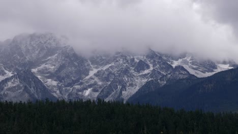 Foggy-Clouds-Over-Dense-Forest-And-Snow-Mountains