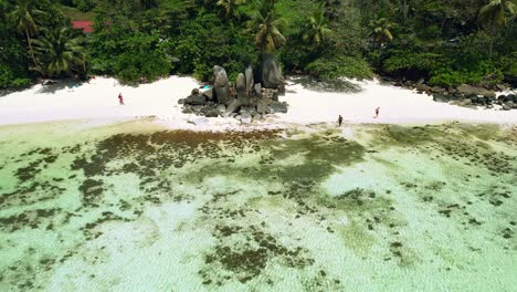 Mahe-Seychelles-reveal-shot-of-people-on-the-beach,-rock-boulders,-low-tide-in-the-morning