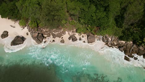 Mahe-Seychelles-bird-eye-view-of-clients-walking-at-the-beach-near-rocks,-give-waves-crashing-on-the-shore