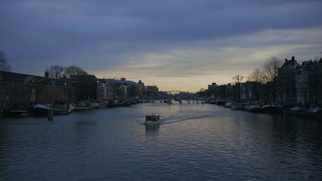 Amsterdam-Amstel-river,-sunset-on-January-2023,-tourist-boat-passing-by