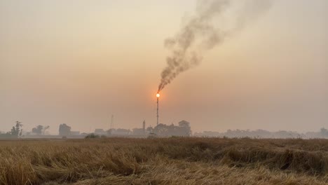 Static-establisher-view-of-industry-area-with-Gas-Plant-tower-releasing-polluting-fumes,-orange-hazy-sunset-sky