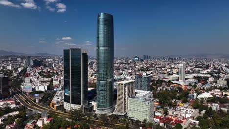 Aerial-view-away-from-the-Mitikah-tower,-in-sunny-Benito-Juárez,-Mexico---pull-back,-drone-shot