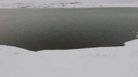 Schneebedecktes-Ozeanufer-Mit-Winterbergen-Im-Hintergrund,-Dolly-Nach-Vorne