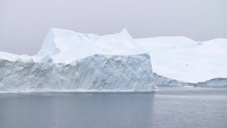 Zeitlupenschwenk-Von-Eisbergen,-Die-An-Einem-Bewölkten-Tag-Mit-Herumfliegenden-Möwen-Auf-Dem-Ozean-Vor-Der-Küste-Grönlands-Schwimmen