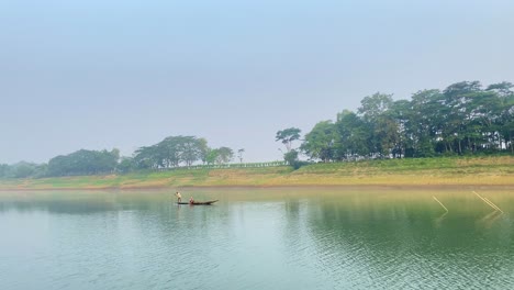 Fishing-boat-in-middle-of-peaceful-river,-Sylhet,-Bangladesh,-fisherman-on-board