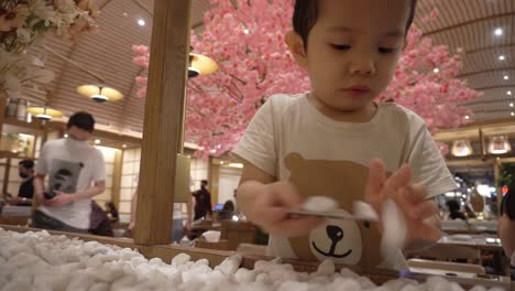 Un-Niño-Indonesio-Chino-De-Tres-Años-Está-Jugando-Con-Adornos-De-Piedra-En-Un-Restaurante-De-Temática-Japonesa