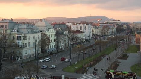 Traffic-on-Dózsa-György-Street,-with-construction-and-the-hills-of-Buda-in-the-background-at-sunset,-Budapest-near-the-Heroes-Square,-Hungary---January-2023