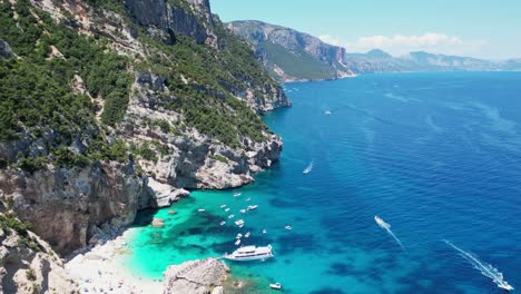 Boat-Tour-Excursion-pick-up-Tourists-at-Cala-Mariolu-Beach,-Baunei-Coast,-Sardinia,-Italy---Aerial-4k