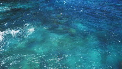 Una-Vista-Fascinante-De-Un-Arrecife-De-Coral-En-Una-Laguna-Azul-Cristalina,-Rodeada-De-Suaves-Olas-Bajo-El-Sol