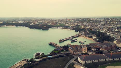 Winter-aerial-drone-flight-over-headland-revealing-fishing-boats-in-Newquay-Harbour-and-town-apartments-in-the-background