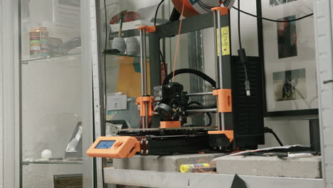 Handheld-Aufnahme-Eines-3D-Druckers-In-Büroräumen,-Der-Ein-Orangefarbenes-Modell-Ausdruckt