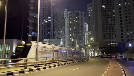 Toma-En-Movimiento-De-Una-Calle-En-Dubai-Por-La-Noche-Mientras-El-Tren-Y-Los-Autos-Pasan