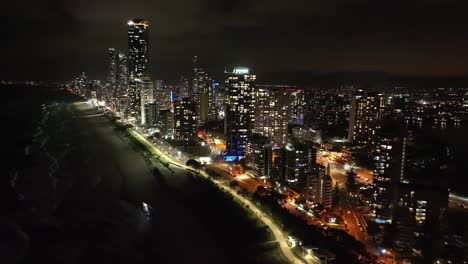 High-flying-drone-footage-showing-amazing-views-of-Surfers-Paradise-at-twilight,-spakling-evening-lights-shining-out-over-breaking-waves-over-iconic-Gold-Coast-beaches