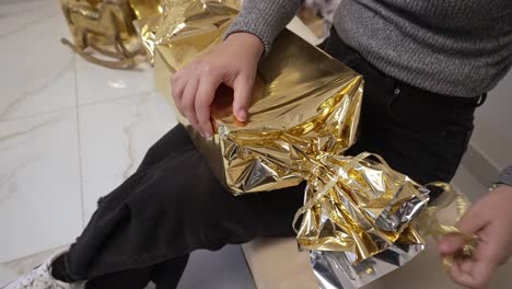 Close-up-of-opening-a-gift-that's-wrapped-in-shiny-gold-paper