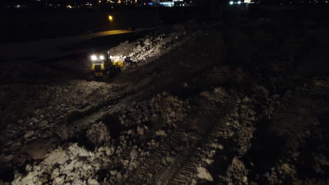 Aerial-footage-of-two-bulldozers-clearing-snow-at-night-during-the-aftermath-of-the-deadly-blizzard-of-2022