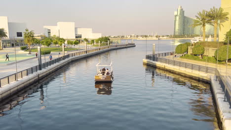 Pequeño-Bote-Navegando-A-Través-De-Un-Canal-Hacia-El-Río-Dubai-Creek,-Cerca-Del-Centro-De-Arte-Jameel