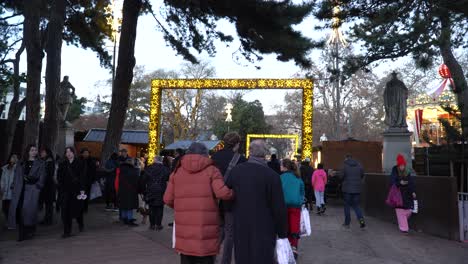 People-walking-through-the-lit-up-arches-at-the-Christmas-village-near-Vienna-town-hall