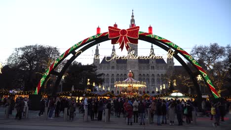 A-busy-Christmas-Village-under-the-Wiener-Christkindlmarkt-sign-opposite-Vienna-Town-Hall,-Austria