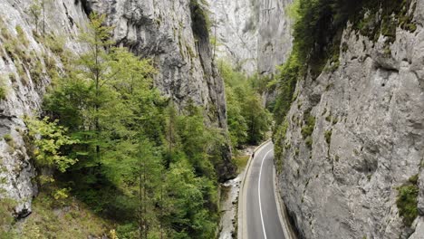 Cars-Driving-On-Narrow-Road-Through-Towering-Cliffs-And-Lush-Greenery