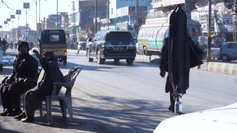 Einheimische-Sitzen-Auf-Stühlen-Am-Straßenrand,-Während-Der-Verkehr-In-Quetta,-Pakistan-Vorbeifährt