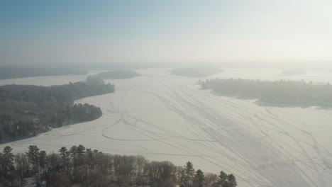 Aerial,-snowmobile-vehicle-tracks-on-a-frozen-lake-covered-in-snow-during-winter