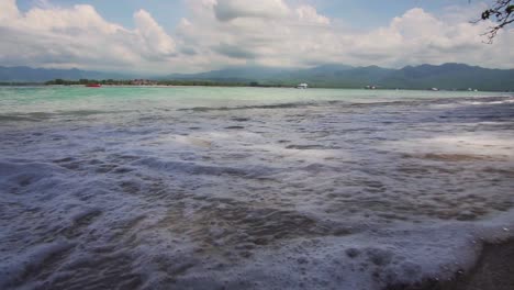 Low-angle-of-small-waves-crashing-and-rolling-over-the-sand-towards-the-camera-on-remote-tropical-beach-in-Bali