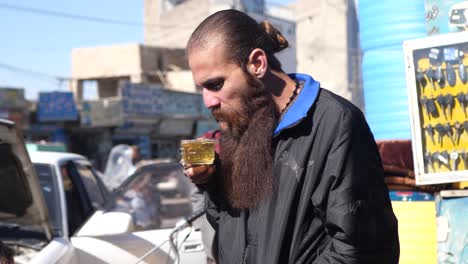 Pakistani-Male-With-Long-Beard-Blowing-On-Hot-Beverage-In-Street-In-Quetta