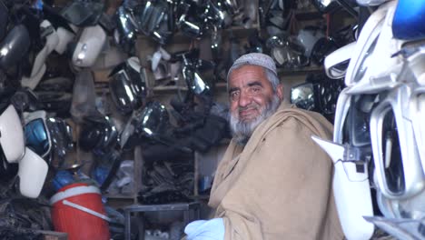 Mayor-Encargado-De-La-Tienda-Sentado-Dentro-De-La-Tienda-De-Automóviles-De-Repuesto-En-Quetta,-Pakistán,-Sonriendo-A-La-Cámara