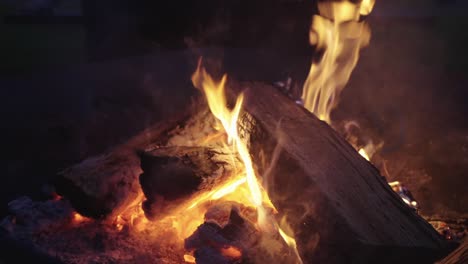 Close-up,-firewood-burning-campfire-outdoors-at-night-with-smoke-coming-out