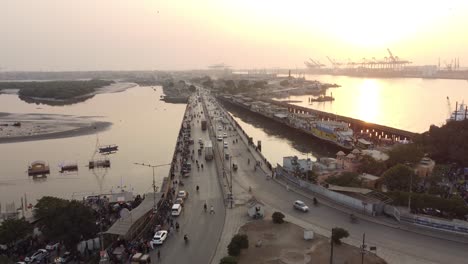 Vista-Aérea-De-La-Carretera-Del-Embarcadero-Nativo-Con-La-Terminal-Portuaria-De-Karachi-En-Segundo-Plano-Durante-La-Puesta-De-Sol