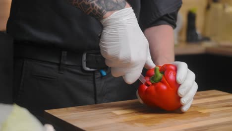 Fresh-red-pepper-being-split-on-a-wooden-board-by-young-professional-male-chef-in-an-elegant-black-shirt-with-tattoos