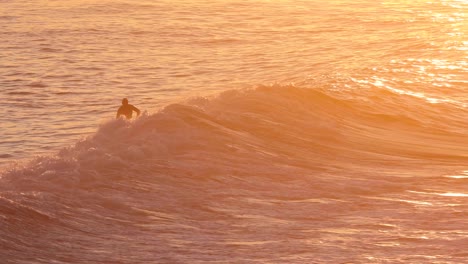 Dieses-Zeitlupenvideo-Zeigt-Einen-Surfer,-Der-Auf-Einer-Meereswelle-Reitet,-Während-Das-Wasser-Im-Sonnenaufgang-Orange-Leuchtet
